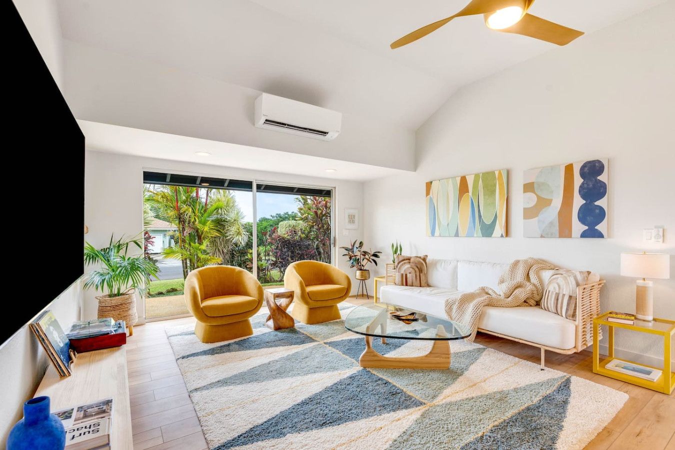 A modern living room with a white sofa, two yellow armchairs, a glass coffee table, and a ceiling fan.