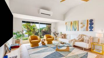 A modern living room with a white sofa, two yellow armchairs, a glass coffee table, and a ceiling fan.