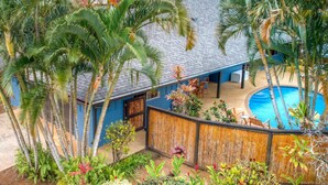 A poolside area with a blue building, palm trees, and a wooden fence. - Cool, Lo-Fi Styled Surf Shack - Ka Hale Nalu (Princeville)