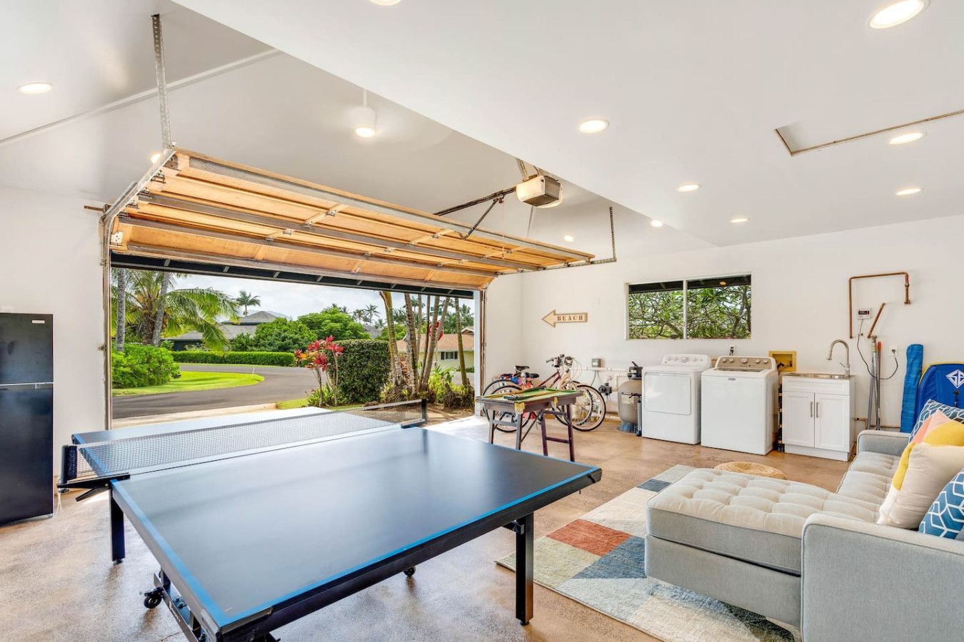 Un espacio de estar moderno con mesa de ping pong, un sofá, zona de cocina y vistas al exterior.