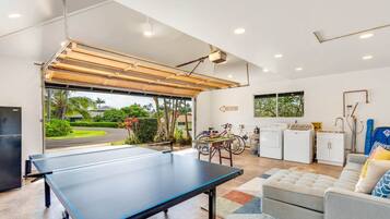 Un espacio de estar moderno con mesa de ping pong, un sofá, zona de cocina y vistas al exterior.