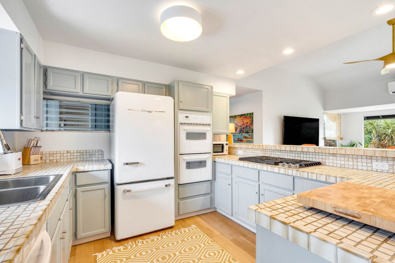 A modern kitchen with white appliances, light blue cabinets, and a patterned rug.