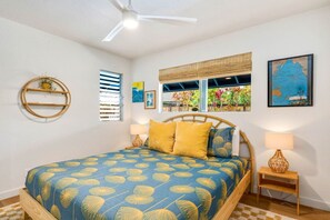 Une chambre à coucher comprenant un lit, un ventilateur de plafond, une fenêtre avec des stores, une étagère fixée au mur et une carte encadrée.