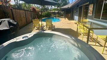 A hot tub with a pool, surrounded by yellow chairs and umbrellas, with a building and palm trees in the background.