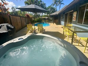 Un bain à remous avec une piscine, entouré de chaises et de parasols jaunes, avec un bâtiment et des palmiers en arrière-plan.