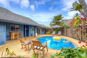 Un jardin avec une piscine, des chaises longues et un coin bar.