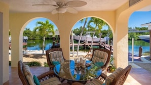 A covered patio with wicker furniture and a glass table, overlooking a marina and water. - Fabulous Island Getaway! Easy access to Florida Bay, Private Beach,  Elevator (Islamorada)