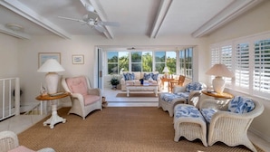 A spacious living room with a large window, a ceiling fan, and wicker furniture. - Fabulous Island Getaway! Easy access to Florida Bay, Private Beach,  Elevator (Islamorada)