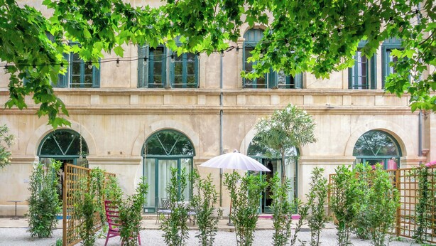 En innergård med en byggnad som har bågformade fönster och en pergola dekorerad med ljusslingor.