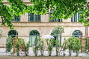 A courtyard with a building featuring arched windows and a pergola with string lights. - Fontedicto - large apartment, courtyard and pool in historic convent, Pézenas (Pézenas)