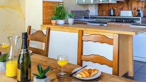 En frukostuppdukning med ett träbord, en flaska champagne, ett glas apelsinjuice, en tallrik med vindruvor och en croissant.