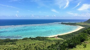 A coastal landscape with a beach, clear turquoise waters, and lush greenery. - Hotel Olive (Ishigaki)