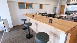Una cocina con una barra de madera, tres taburetes, un lavaplatos de acero inoxidable y un refrigerador.