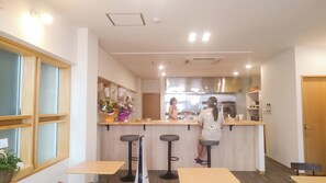 A restaurant interior with a counter, stools, and a kitchen area. - Hotel Olive (Ishigaki)