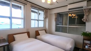 Habitación de hotel con dos camas, ventanas amplias, aire acondicionado y vista al mar.