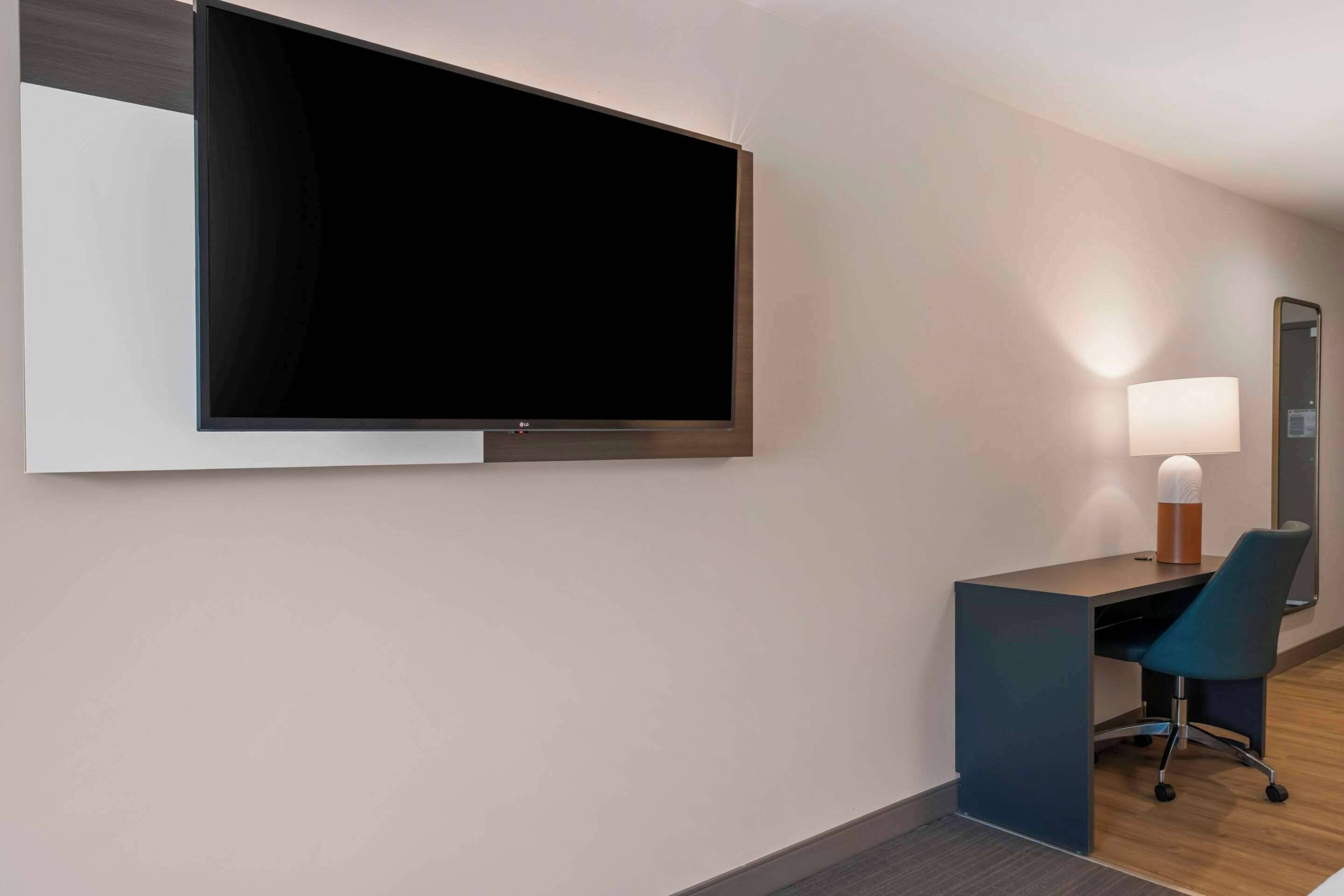Una habitación de hotel moderna con un televisor de pantalla plana grande montado en la pared, un escritorio con una silla y una lámpara de noche.