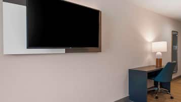 Una habitación de hotel moderna con un televisor de pantalla plana grande montado en la pared, un escritorio con una silla y una lámpara de noche.