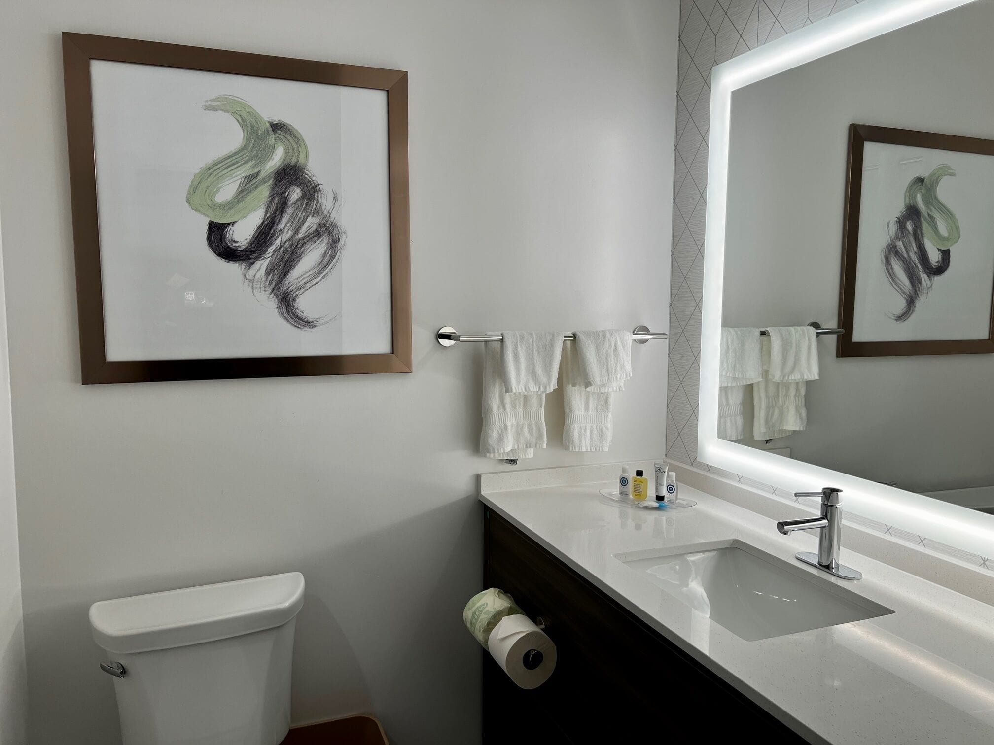 A modern bathroom with a white sink, a toilet, and a framed abstract artwork on the wall.