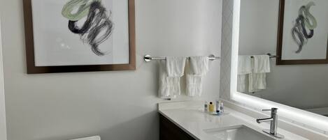 Une salle de bain moderne avec un lavabo blanc, des toilettes et une œuvre d’art abstraite encadrée accrochée au mur.