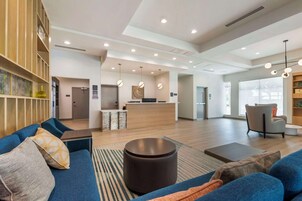 Un'ampia hall d'albergo con reception, area relax con divani e un'ampia finestra che lascia entrare luce naturale.