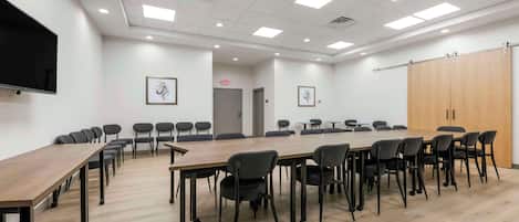 A conference room with a long table, chairs, a flat-screen TV, framed artwork, and a wooden wardrobe.