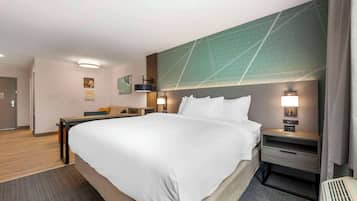 A hotel room with a large bed, a desk, a chair, and a nightstand with a lamp.