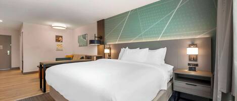 A hotel room with a large bed, a desk, a chair, and a nightstand with a lamp.
