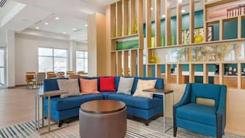 A modern hotel lobby with a blue sofa, a round ottoman, and a blue armchair. There are wooden shelves with decorative items and a painting.