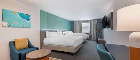 A hotel room with a bed, two chairs, a small table, a TV, and a painting on the wall.