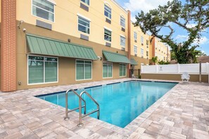 A swimming pool with a metal ladder, surrounded by a brick patio.
