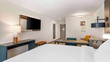 A hotel room with a bed, a desk, a chair, a TV, and a lamp.
