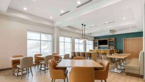 A spacious dining area with a long table and multiple chairs, a bar area with shelves of bottles, and a seating area with a sofa and chairs. - Comfort Suites St. Augustine Historic District Area (St. Augustine)