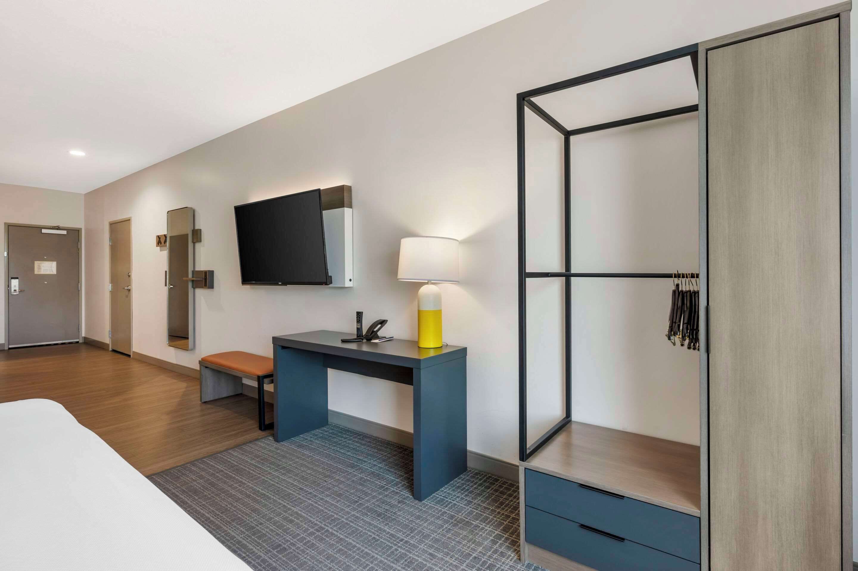 Una habitación de hotel moderna con cama, escritorio con lámpara, televisión y armario.