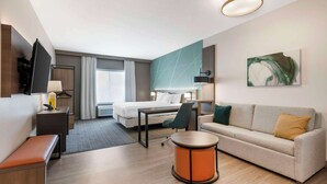 A modern hotel room with a bed, sofa, desk, and a round orange table. - Comfort Suites Richmond East (Richmond)