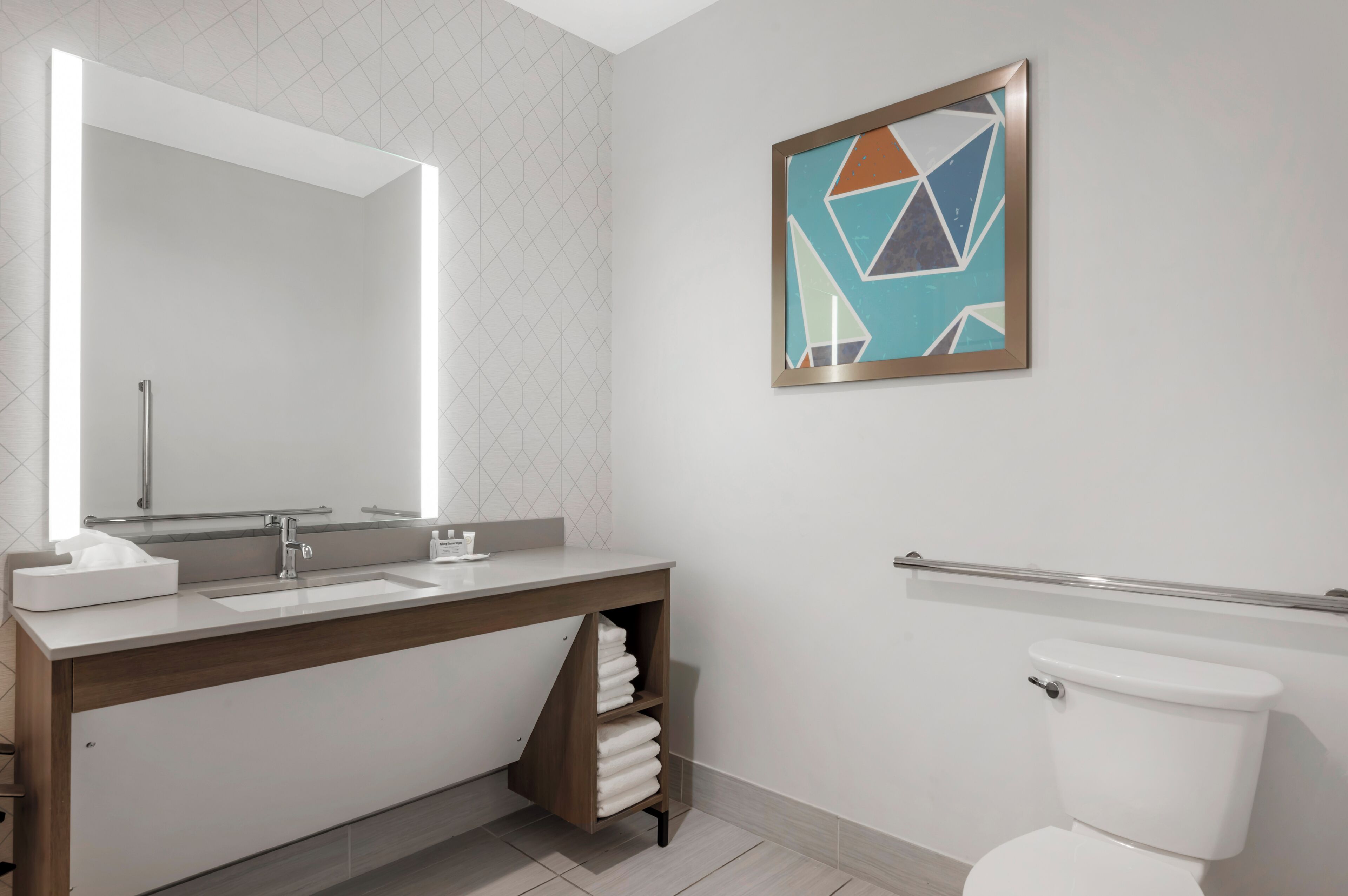 Un baño moderno con un espejo grande, un lavamanos, un inodoro y un perchero para toallas.