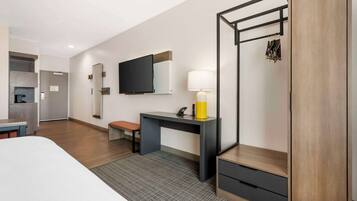 Et moderne hotelværelse med seng, skrivebord med lampe, fjernsyn og garderobeskab.
