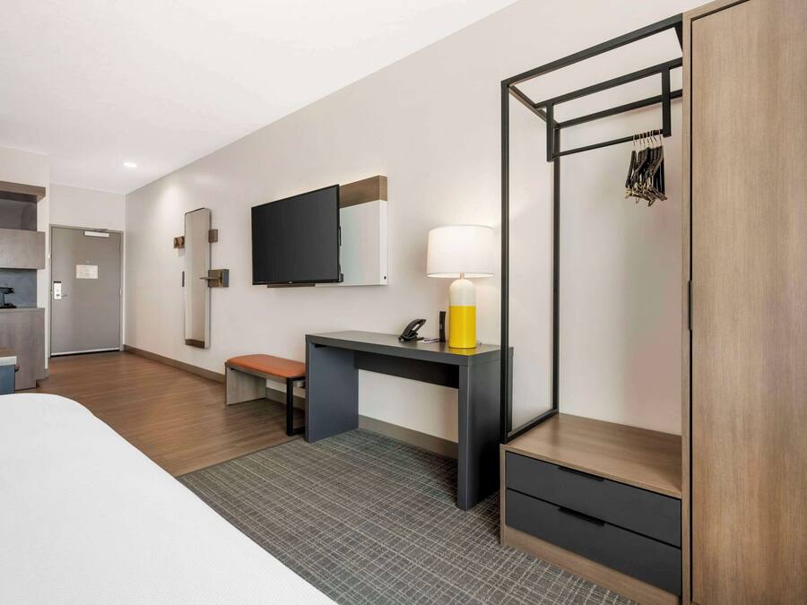 Et moderne hotelværelse med seng, skrivebord med lampe, fjernsyn og garderobeskab.