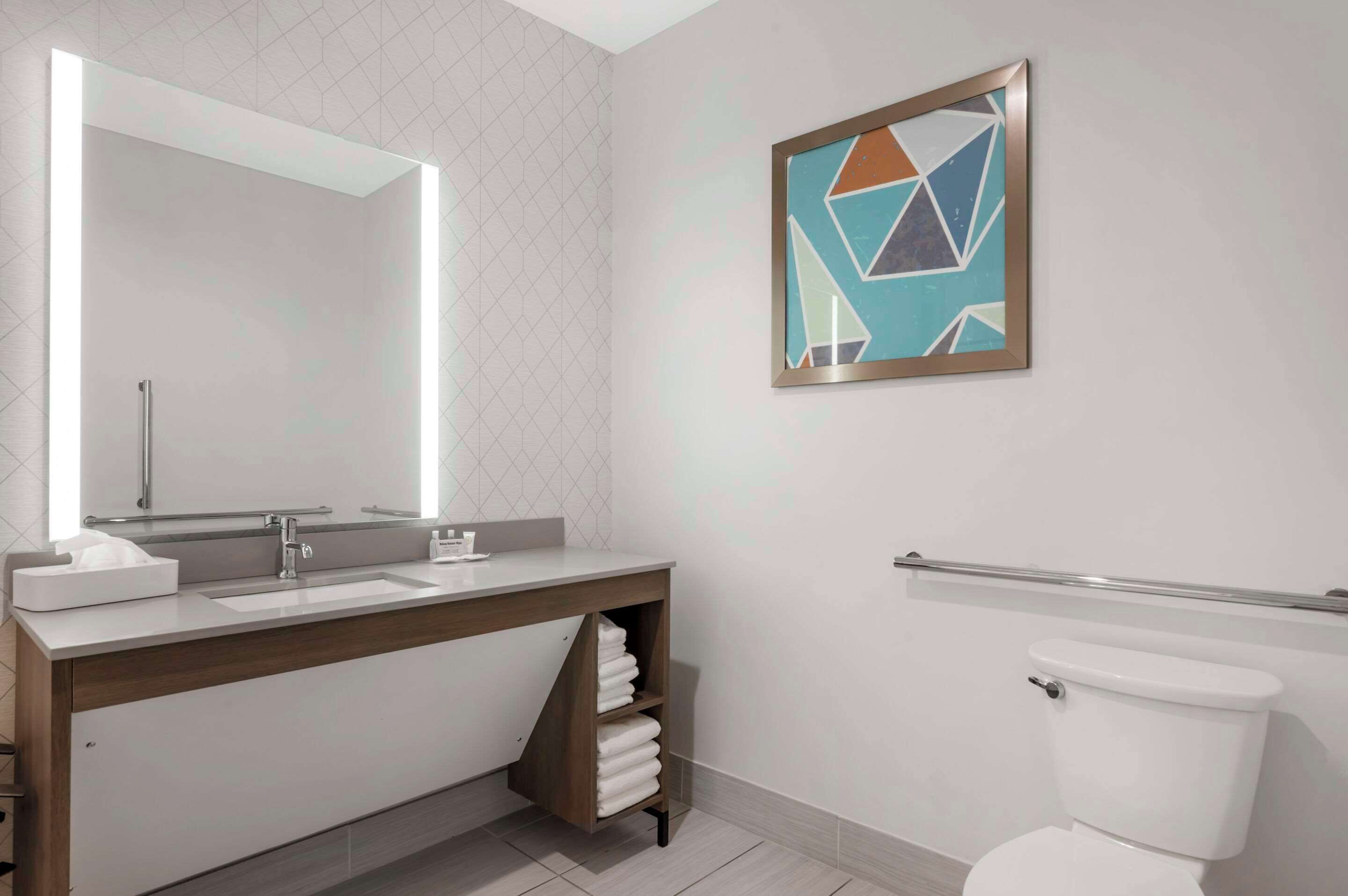 A modern bathroom with a large mirror, a sink with a towel rack, and a toilet.