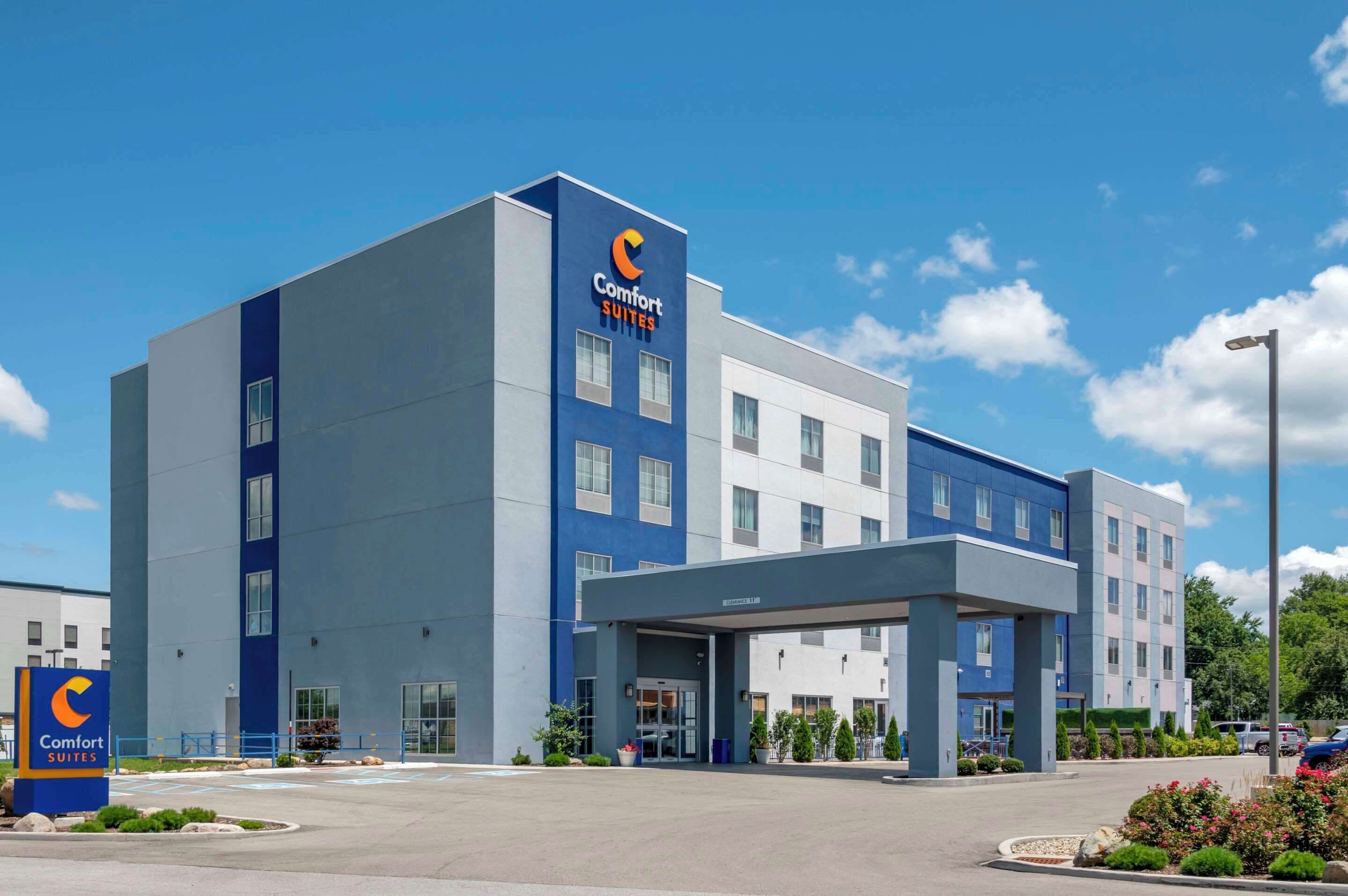 A modern Comfort Suites hotel with a blue and white facade, a covered entrance, and a parking lot.