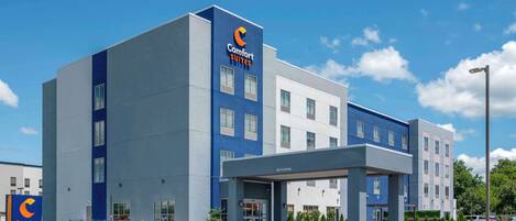 A modern Comfort Suites hotel with a blue and white facade, a covered entrance, and a parking lot.
