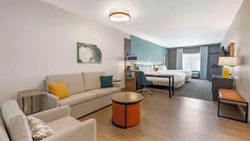 Una habitación de hotel moderna con sofá, sillón, mesa redonda y cama con cabecero.