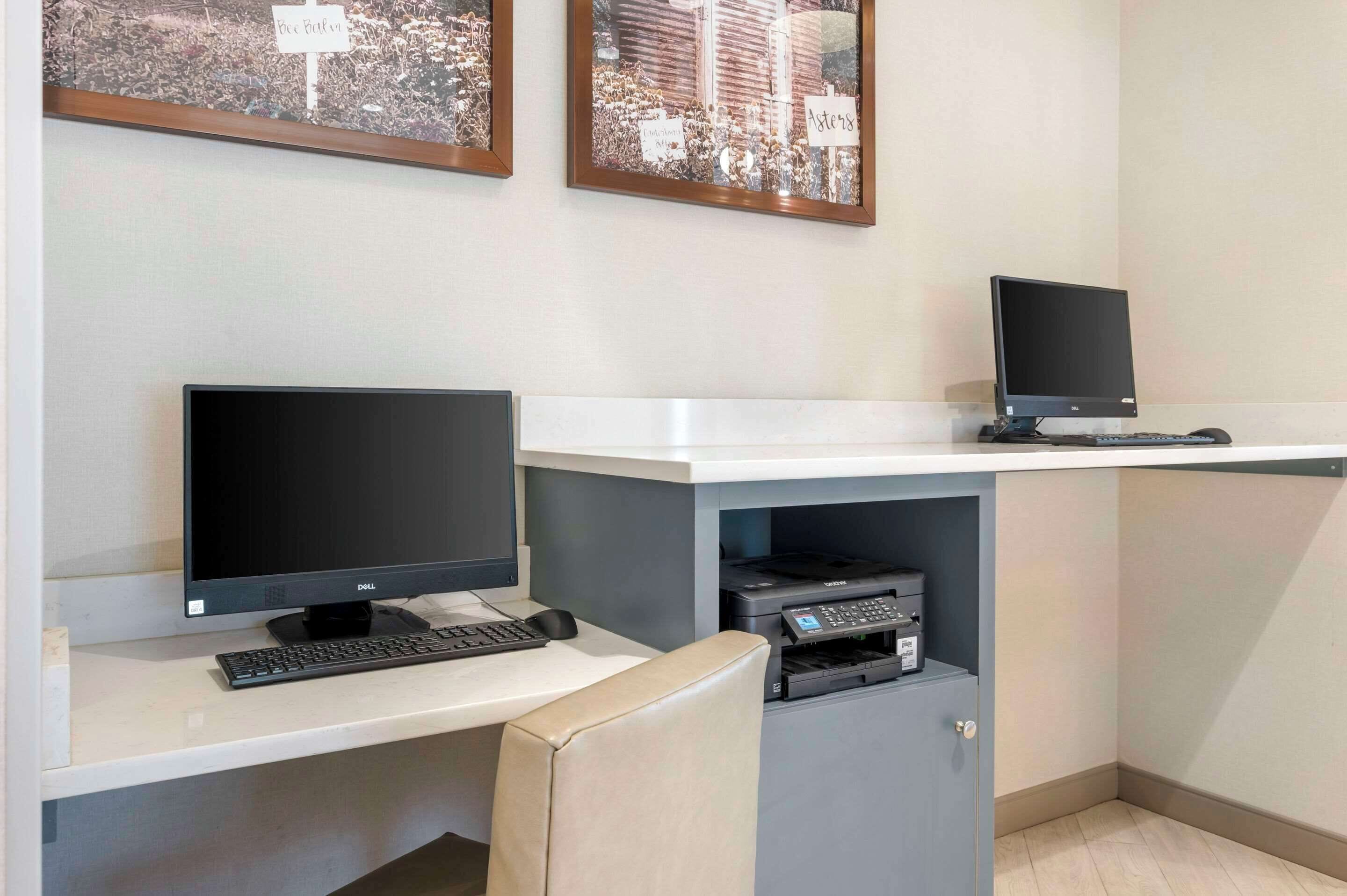 Un espai de treball amb dos monitors, un teclat i una impressora sobre una taula.