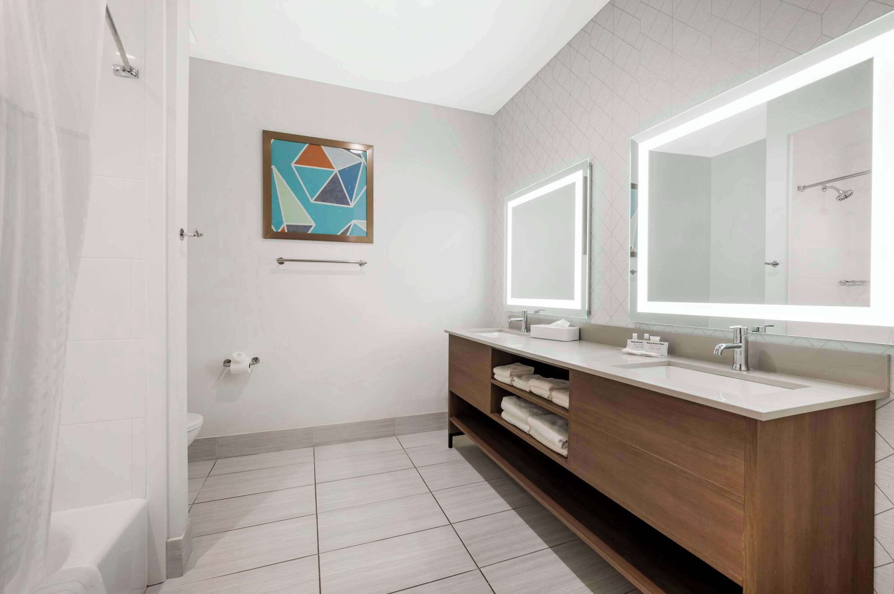 A modern bathroom with a large mirror, two sinks, a towel rack, and a shower.