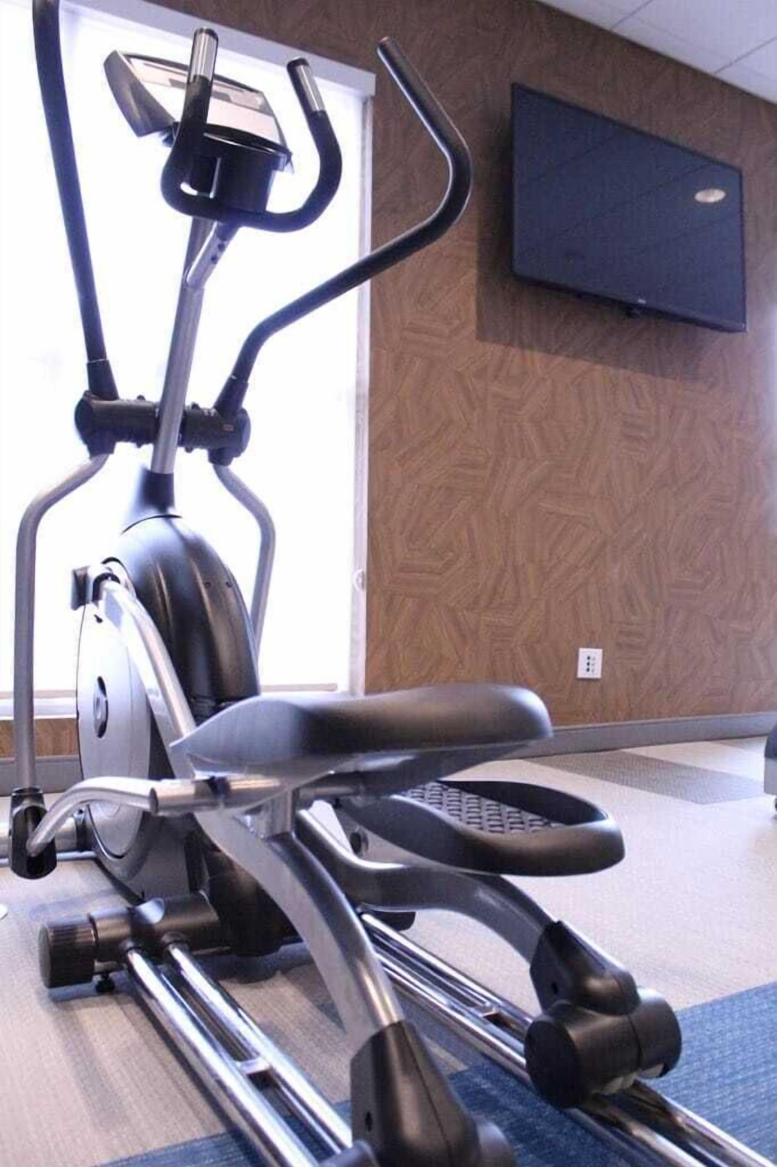 An exercise machine in a room with a patterned wall and a flat-screen TV mounted on the wall.