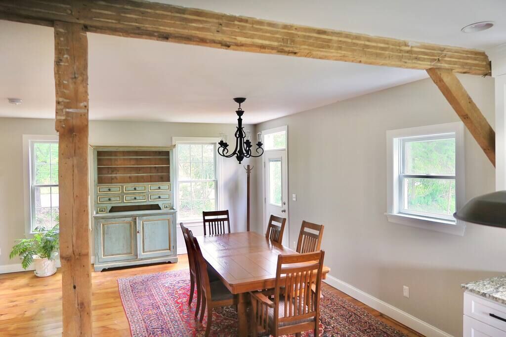 A dining area with a wooden table and chairs, a chandelier, and a large window.