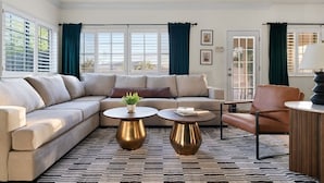 Un salon moderne avec un canapé d’angle beige, deux tables basses rondes, un fauteuil en cuir et un tapis à motifs.