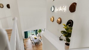 Un intérieur moderne avec un escalier, un coin repas et un mur décoré de chapeaux et d’un panneau néon.