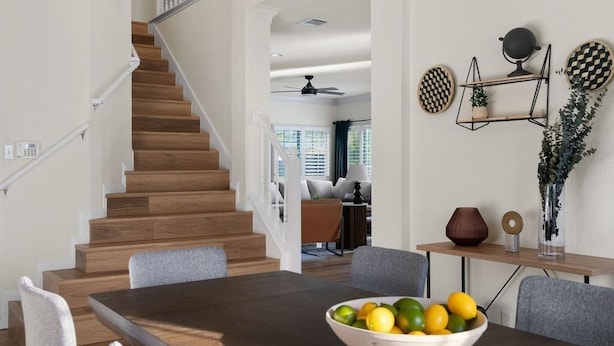 Un espace repas moderne avec une table et des chaises en bois, un saladier rempli de fruits et un escalier menant à une autre pièce.