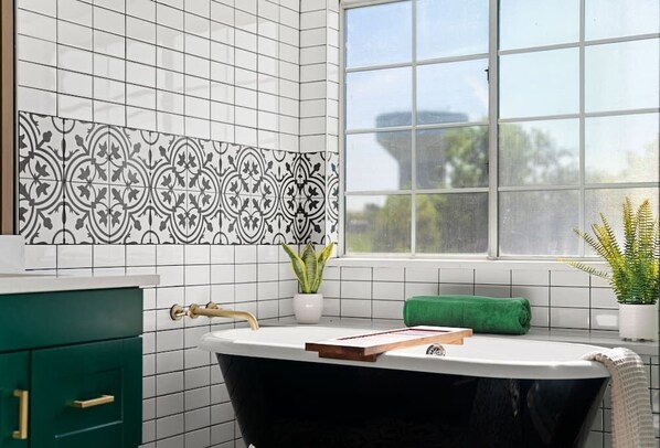Une salle de bain avec une baignoire noire, des carreaux blancs, une fenêtre et une serviette verte.
