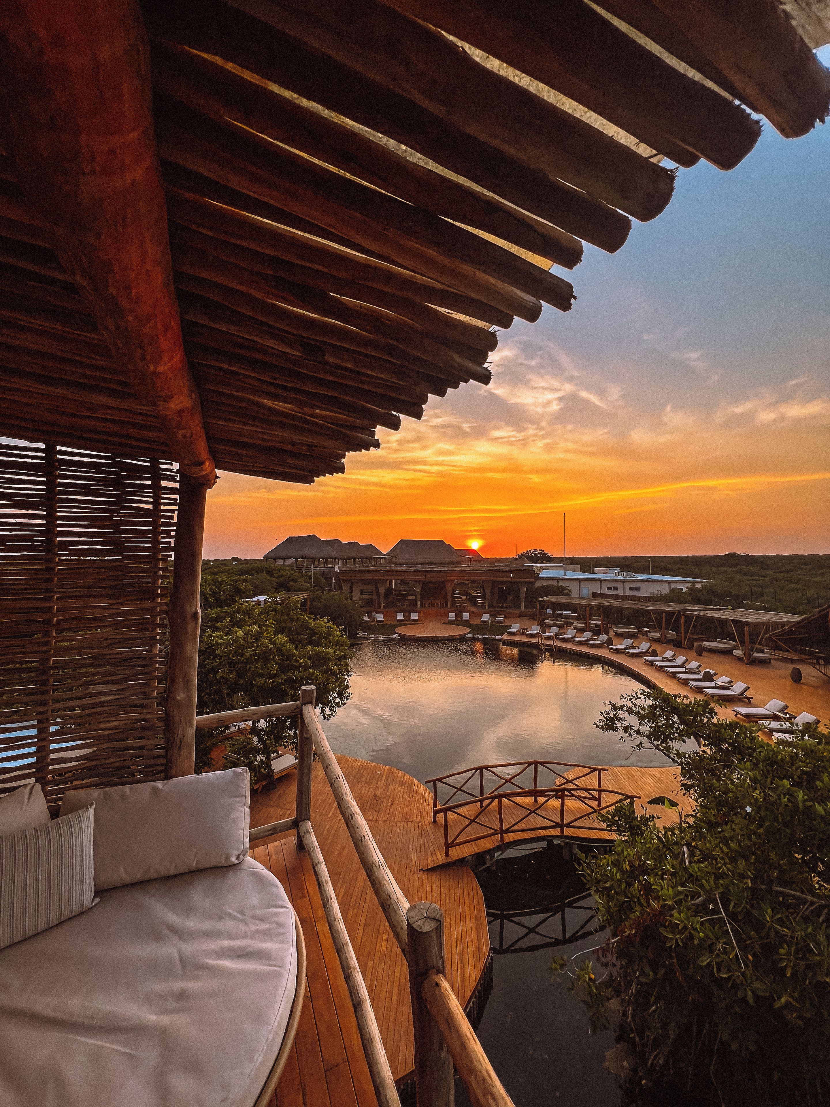 A wooden deck with a pool, lounge chairs, and a sunset view.